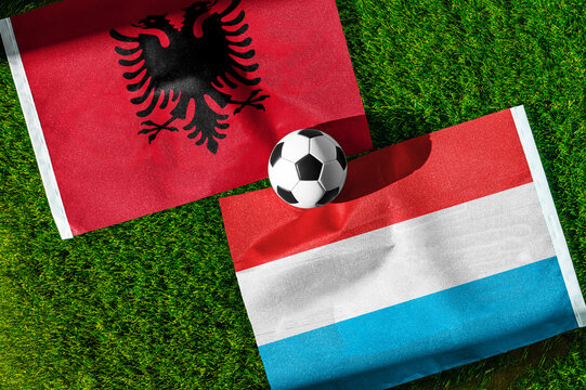 Albania vs. Luxembourg football match. National flags on green grass with soccer ball in the middle. Football background for international match.