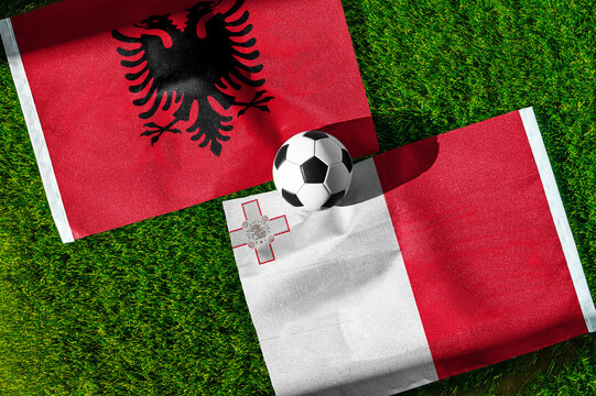 Albania vs. Malta football match. National flags on green grass with soccer ball in the middle. Football background for international match.