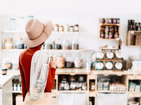 A caucasian female shopper stands with her back to the camera, looking at organic goods on wooden shelves inside a bright modern store interior. 