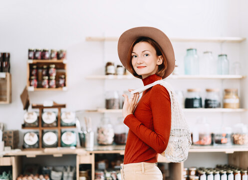 A caucasian female shopper buys organic goods using reusable containers inside a modern bulk grocery store. Sustainable lifestyle and conscious consumer behavior concept.