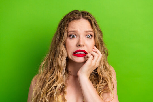Glamorous young woman with blonde hair biting lip against bright green background