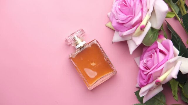 Glass perfume bottle with pink roses on light background cinematic top view close up footage