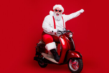 Naklejka premium Santa Claus on a red scooter celebrating Christmas with festive outfit and sunglasses in a fun holiday portrait