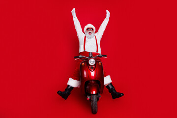 Naklejka premium Santa Claus riding a red scooter with arms raised against a red background, a festive Christmas portrait showing joy, celebration and playful holiday spirit