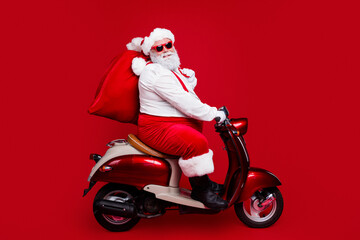 Naklejka premium Santa Claus riding a red vintage scooter with a large gift sack, wearing sunglasses and festive suit on a bold red background