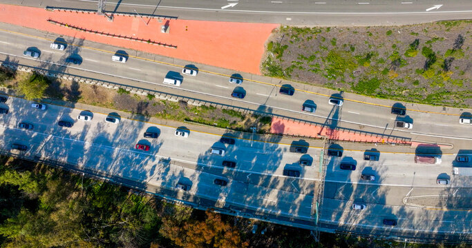 Aerial view of a busy multi-lane highway with cars driving through a landscape with trees and shadows cast by overhead structures in Los Angeles, California, United States.