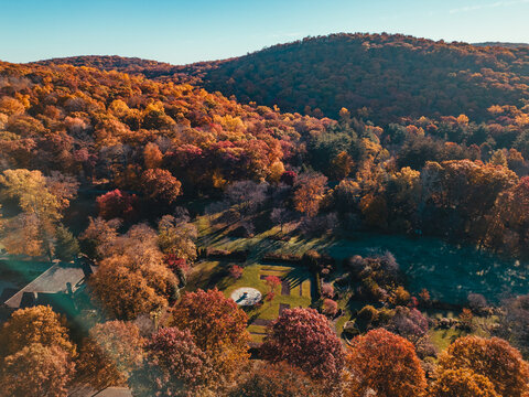 Aerial view of vibrant autumn foliage covering rolling hills with a small garden clearing and a building corner in New Jersey, United States.