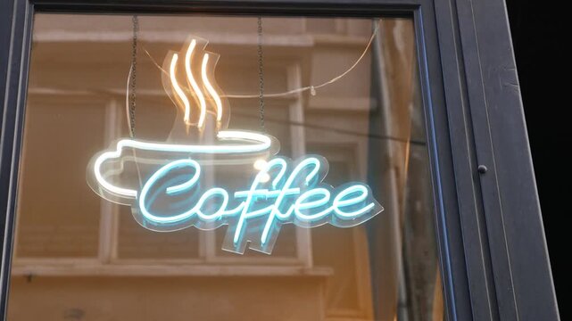 Neon coffee sign glowing on cafe window in evening city street atmosphere with cinematic reflection