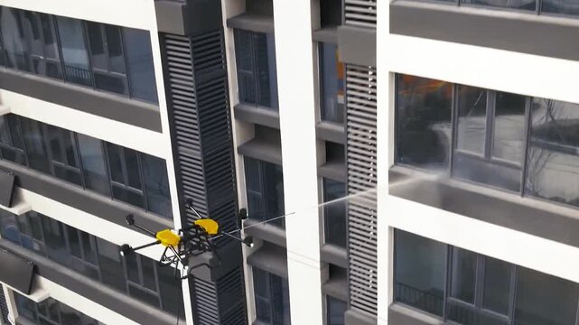 Innovative drone with smart technology providing window cleaning service for a high rise building. Automatic washer spraying water on glass, ensuring efficient and safe maintenance