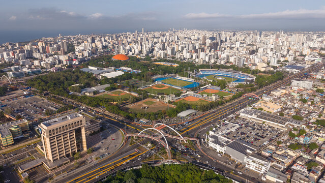 Aerial view of the Centro Olimpico Juan Pablo Duarte sports complex, surrounding high-rise buildings, and a modern pedestrian bridge in Santo Domingo, Distrito Nacional, Dominican Republic.
