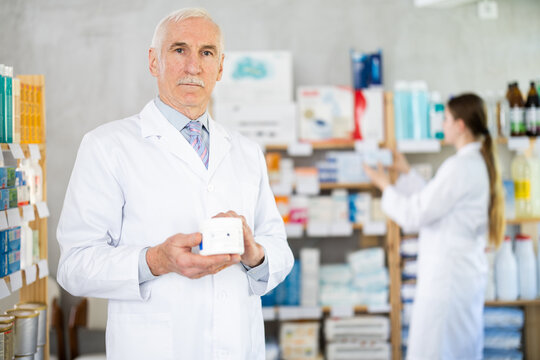 Mature male pharmacist offering cream while woman apothecary working in drugstore
