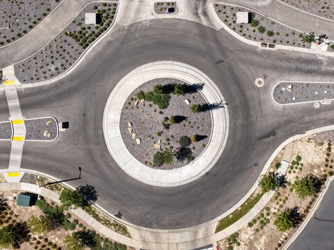 Aerial view of a modern roundabout in Silicon Slopes featuring landscaped center with rocks and shrubs, surrounded by asphalt roads and sidewalks in Lehi, Utah, United States.