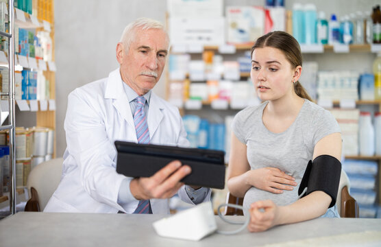 Pregnant woman having blood pressure measured by male pharmacist holding tablet
