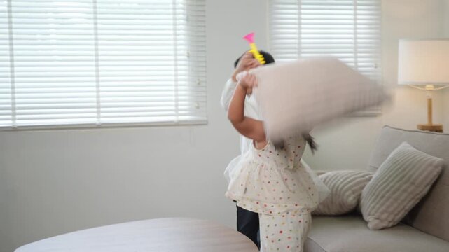 Playful asian siblings having a pillow fight and tickling each other on the sofa in the living room at home