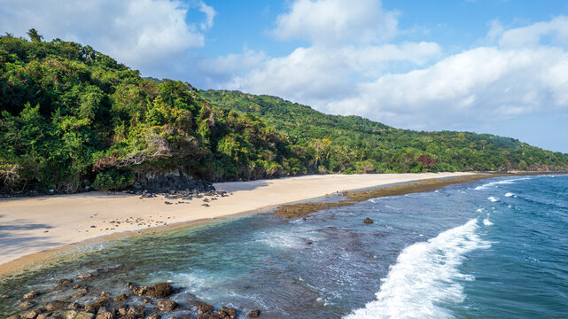 Aerial view of a pristine sandy beach bordered by lush green hills and rocky formations along the coastline in Bajawa, Nusa Tenggara Timur, Indonesia.