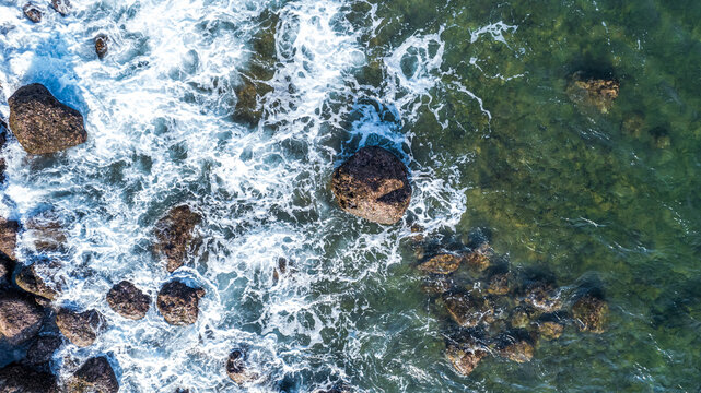 Aerial view of ocean waves crashing against dark rocks along the coastline in Bajawa, Nusa Tenggara Timur, Indonesia.