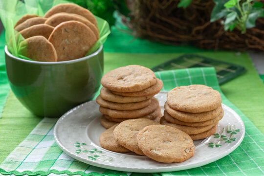 Cookies on a shamrock plate with a bowl of cookies beside them on a green tablecloth in a bright setting