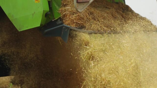 Combine harvester ejecting chopped straw during harvesting in a field, slow motion close-up of agricultural machinery