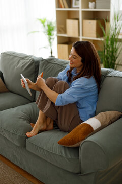 Young woman enjoying easy online shopping from home, holding a digital tablet and credit card while sitting comfortably on a sofa, making secure e-commerce purchases