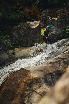 Canyoning adventurer rappelling down a cascading rocky waterfall