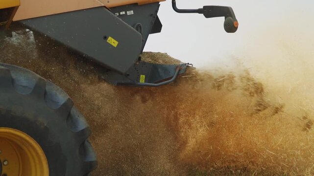 Combine harvester spreading straw and chaff across a field during harvest in slow motion with dust rising in the air