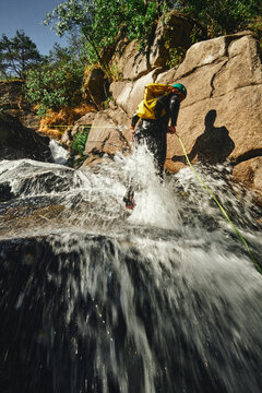Canyoning adventurer rappelling down a powerful cascading waterfall