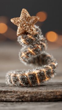A spiral Christmas tree decoration with a glittery star on top sits on a wooden surface with a blurred bokeh background.