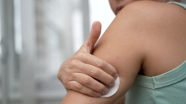 Close-up of a female patient attaching a continuous glucose monitoring sensor to the back of her upper arm using an automatic applicator at home.