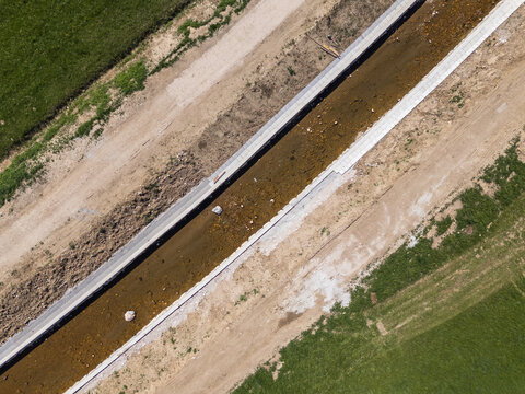Aerial view of a river undergoing restoration with channel widening and flood protection measures in place near open land.