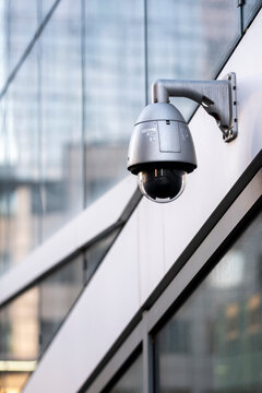 Security camera on a modern glass building where the camera and architecture create an urban technology and surveillance concept around the building