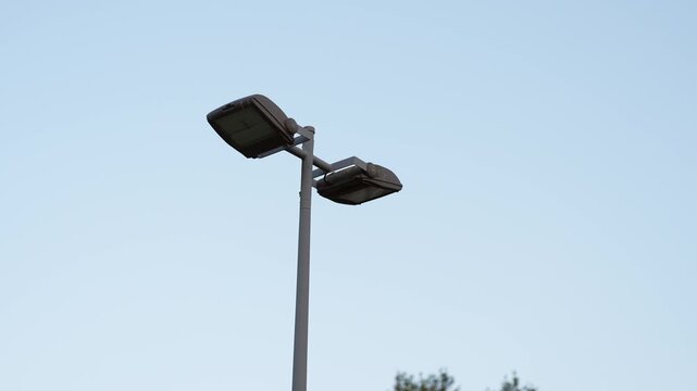Weathered twin lamp streetlight fixture standing against a clear blue daytime sky, vintage urban public lighting with minimalist composition