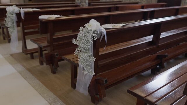 Church pews adorned with white flowers and ribbon for a wedding ceremony, ready for guests attending the sacred event