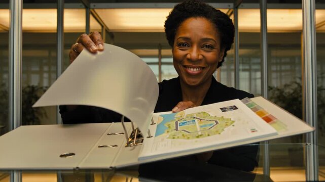 Reaching into binder, woman in blazer flipping pages at glass desk, revealing color-coded plan