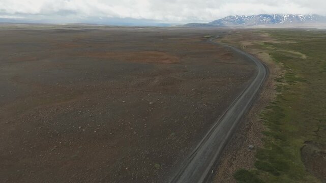 An aerial drone shot of the remote F35 gravel road winding through the desolate volcanic landscape of the Iceland highlands under a cloudy sky.