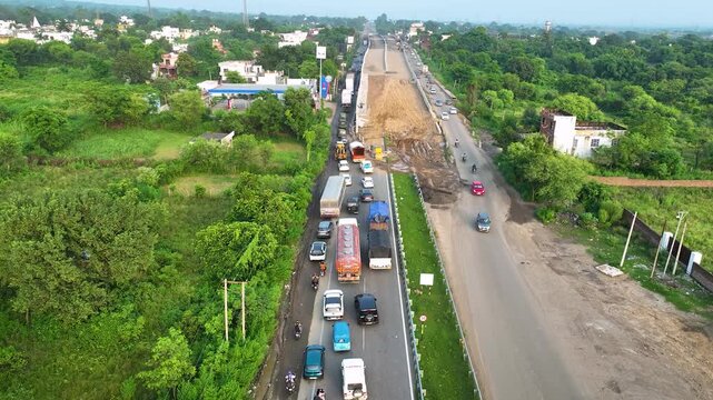 4K aerial tracking shot of severe highway traffic congestion caused by active flyover construction and elevated bridge infrastructure upgrades in India.
