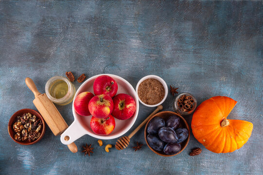 Fall baking, cooking seasonal dessert background with various ingredients - honey, pumpkin squash, brown sugar, cinnamon, spices, red apples, plums, walnuts, pecans. Autumn, thanksgiving bakery backgr