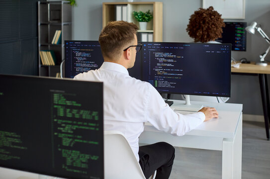 Programmer developer coding software on computer monitors. Back view shows focused engineer at dual screens, reviewing code and running tests. Concept shows modern software teamwork and focus.