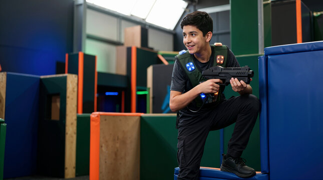 Teenage boy playing laser tag in an indoor arena. Young male holding a game gun vest during interactive entertainment activity. Modern indoor recreation and youth game concept