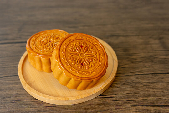 Two mooncakes on bamboo wooden plate on wooden table, tradition Chinese moon cake, sweet dessert for mid autumn celebration. Happy Chinese translation mid autumn festival.