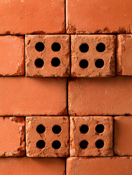 Close-up full frame shot of stacked orange red clay perforated bricks wall, featuring four holes texture pattern for masonry construction, building material, and architectural background.