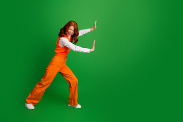 Woman in orange outfit pushing an invisible wall with playful expression against a bright green...