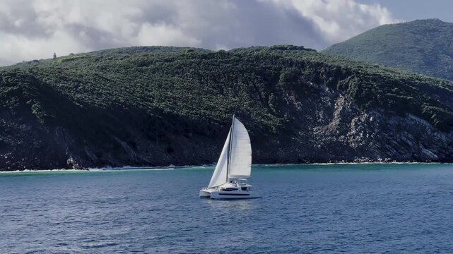 White Catamaran Sailing Near Rocky Coastal Cliffs