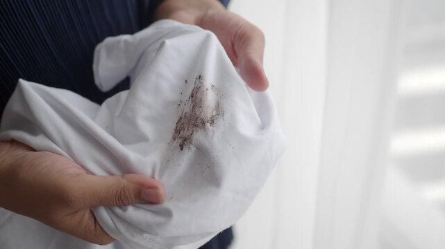 Close up of hands holding white fabric with dark dirt stain close up detail