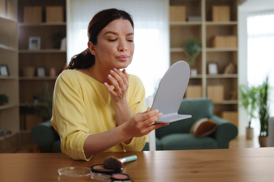 Woman checking skin condition in mirror, doing daily beauty routine, applying cosmetics for a glowing facial complexion and healthy appearance