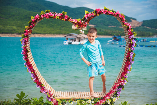 A happy boy schoolchild is posing by the beach by the sea during a summer vacation at tropical resort