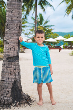 happy boy schoolchild posing by a palm tree on beach by the sea during a summer vacation at a tropical resort