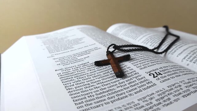 Christian concept with a small wooden cross necklace resting on the pages of the holy bible. The camera glides over the verses of the sacred text, creating a reflective and spiritual mood