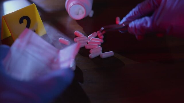 Forensic evidence bagging, gloved hands using tweezers to put a white pill into a plastic bag near a yellow marker on a wooden table under window frame shadows and police lights.