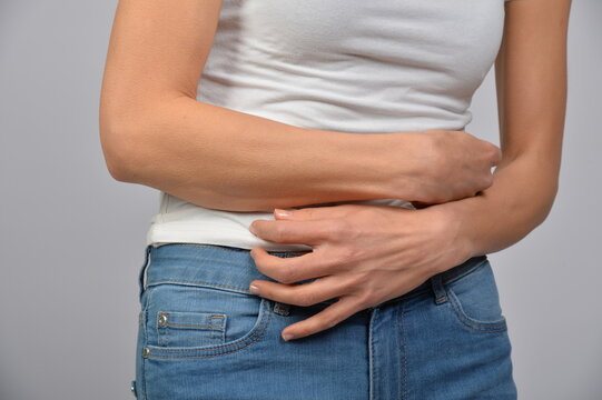 Frau h&auml;lt sich den Unterbauch mit beiden H&auml;nden. Symbol f&uuml;r Bauchschmerzen, Verdauungsbeschwerden, Menstruation, Kr&auml;mpfe, Unwohlsein, Gesundheit und medizinische Beschwerden.