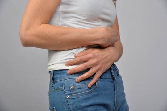 Frau h&auml;lt sich den Unterbauch mit beiden H&auml;nden. Symbol f&uuml;r Bauchschmerzen, Verdauungsbeschwerden, Menstruation, Kr&auml;mpfe, Unwohlsein, Gesundheit und medizinische Beschwerden.